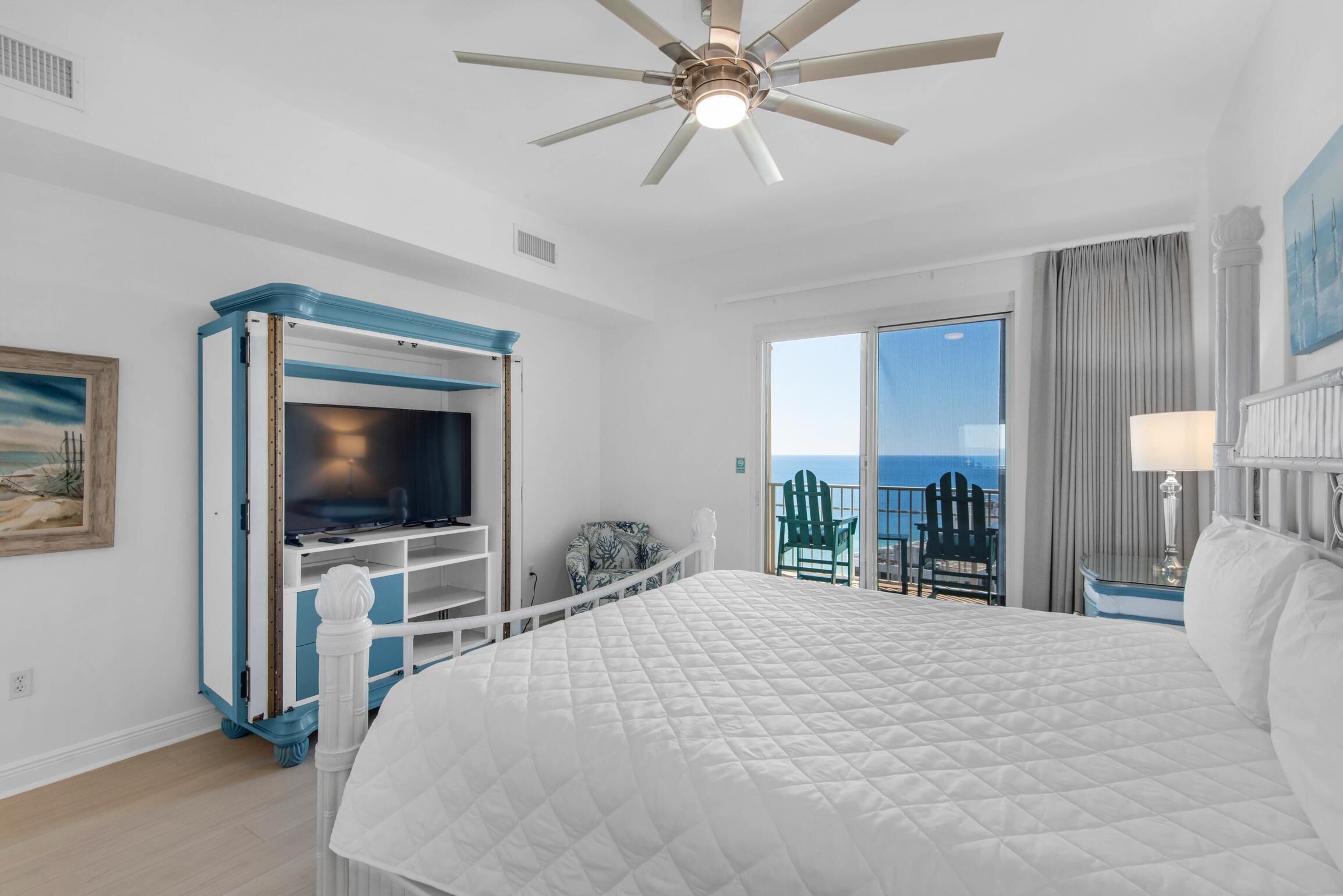 Habitación de hotel con una cama grande, ventilador de techo, televisor y balcón con vista al océano.