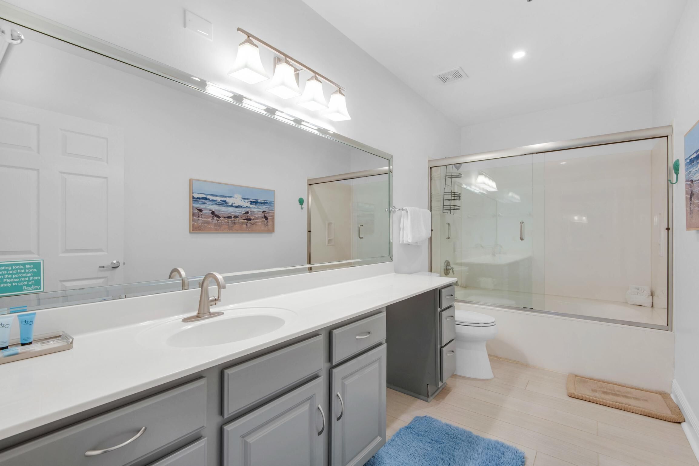 A modern bathroom with a large mirror, a white sink, a toilet, and a glass shower enclosure.