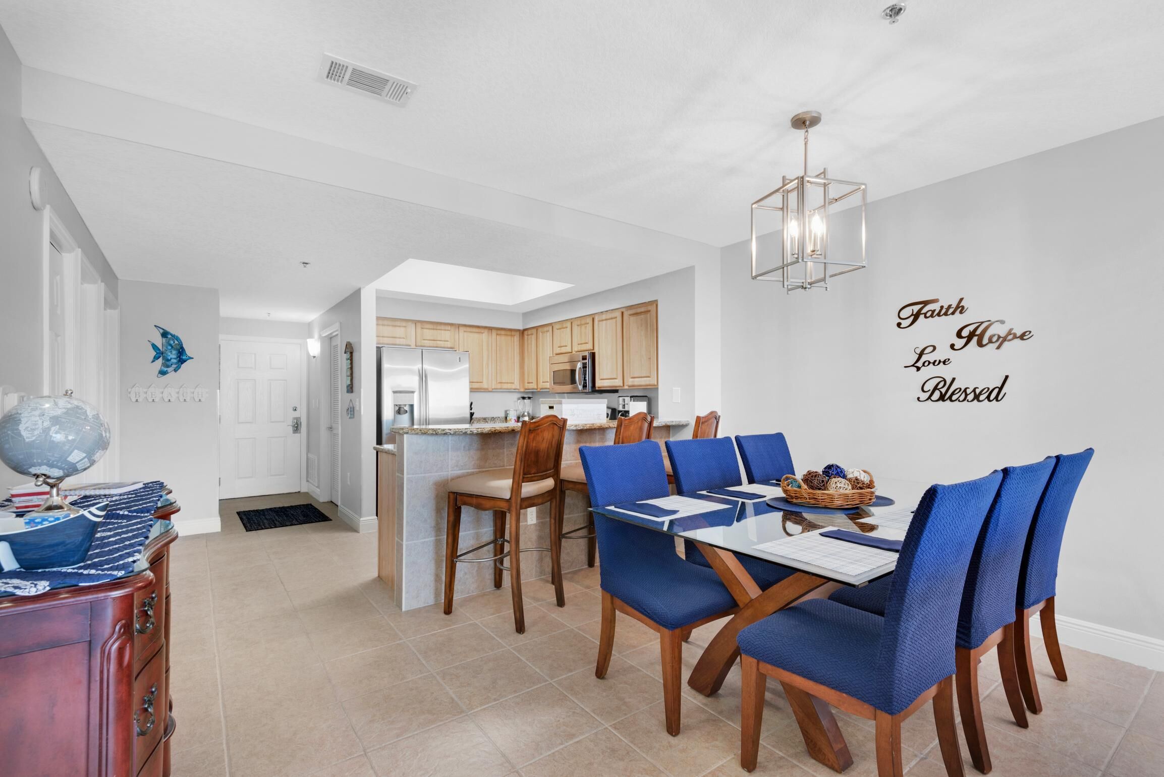 A modern kitchen with wooden cabinets, a central island, and a dining area with blue chairs.