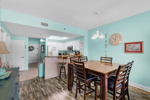 A spacious kitchen with white cabinets, a dining area with a wooden table and chairs, and a light blue wall. - Ariel Dunes I 2202 (Miramar Beach)