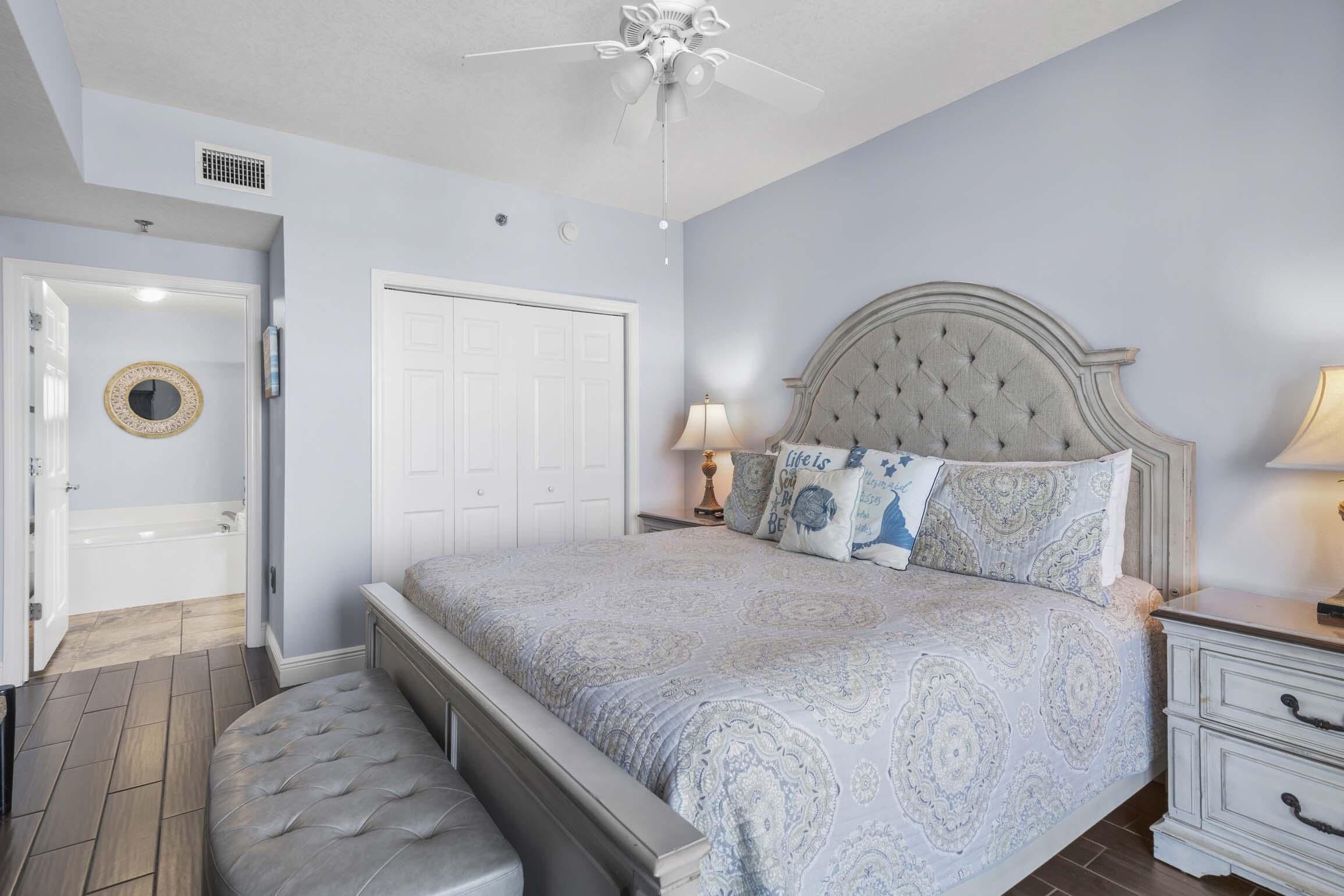 A bedroom with a tufted headboard, a large bed with patterned bedding, a bedside table with a lamp, and a bench at the foot of the bed.