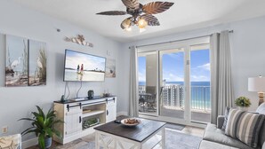 A spacious living room with a large TV, a ceiling fan, and a balcony with a view of the ocean. - Ariel Dunes I 2009 (Miramar Beach)