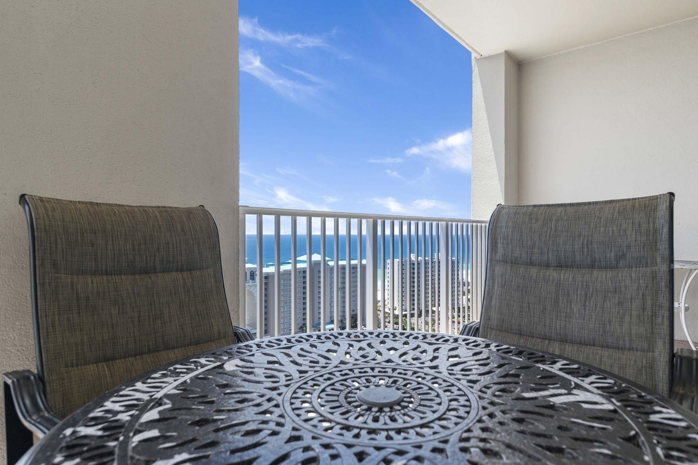 Ein Balkon mit zwei Stühlen und einem Tisch, mit Blick auf einen Strand und hohe Geb äude.