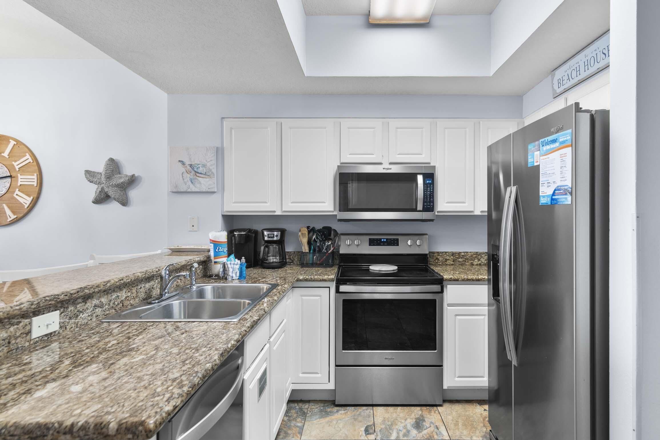A modern kitchen with white cabinets, stainless steel appliances, granite countertops, and a clock on the wall.