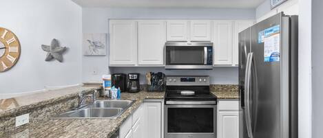 A modern kitchen with white cabinets, stainless steel appliances, granite countertops, and a clock on the wall.