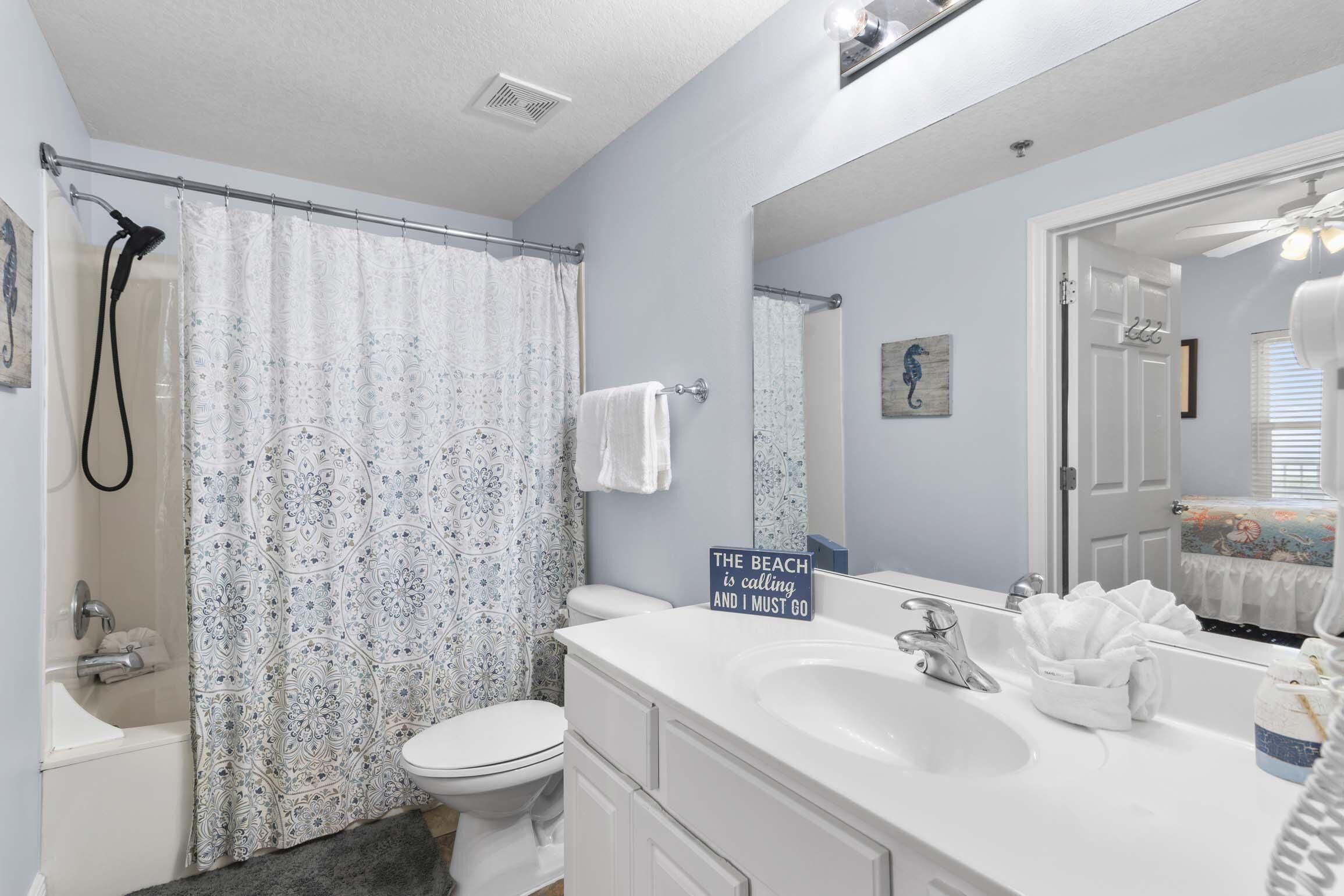 A bathroom with a shower, toilet, and sink. There is a sign on the wall that reads "The beach is calling and I must go."