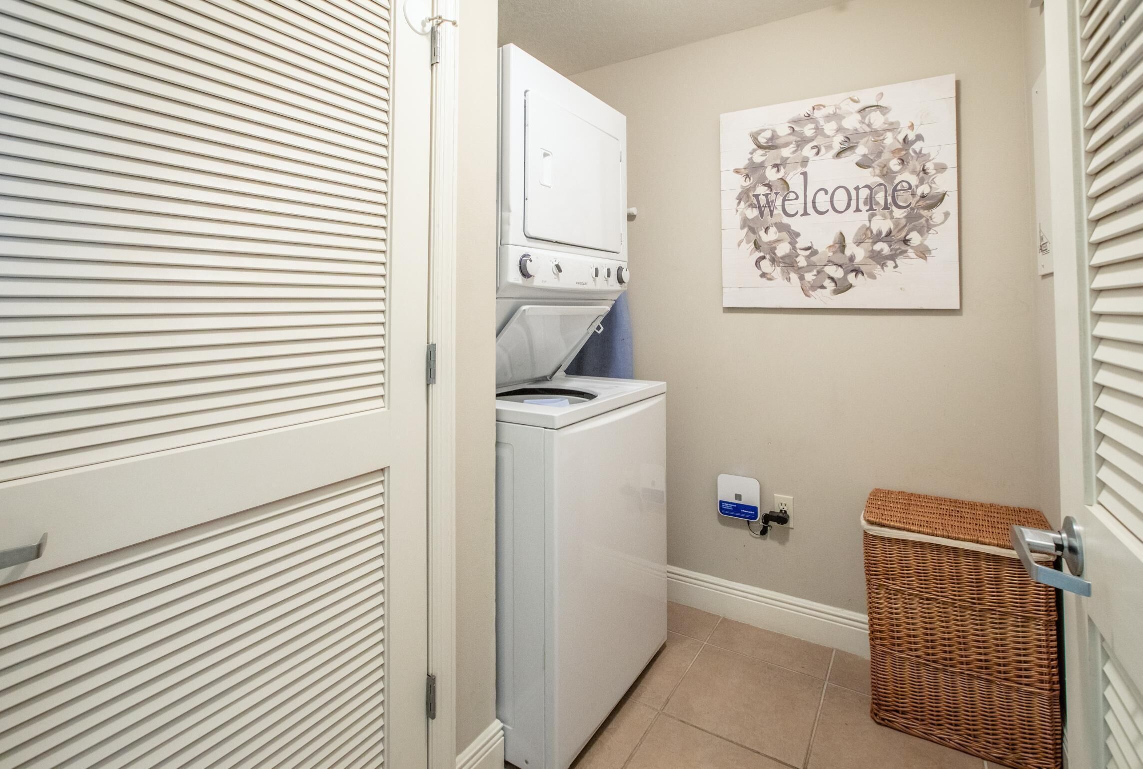 A laundry room with a washing machine, a drying machine, a wicker basket, and a welcome sign on the wall.