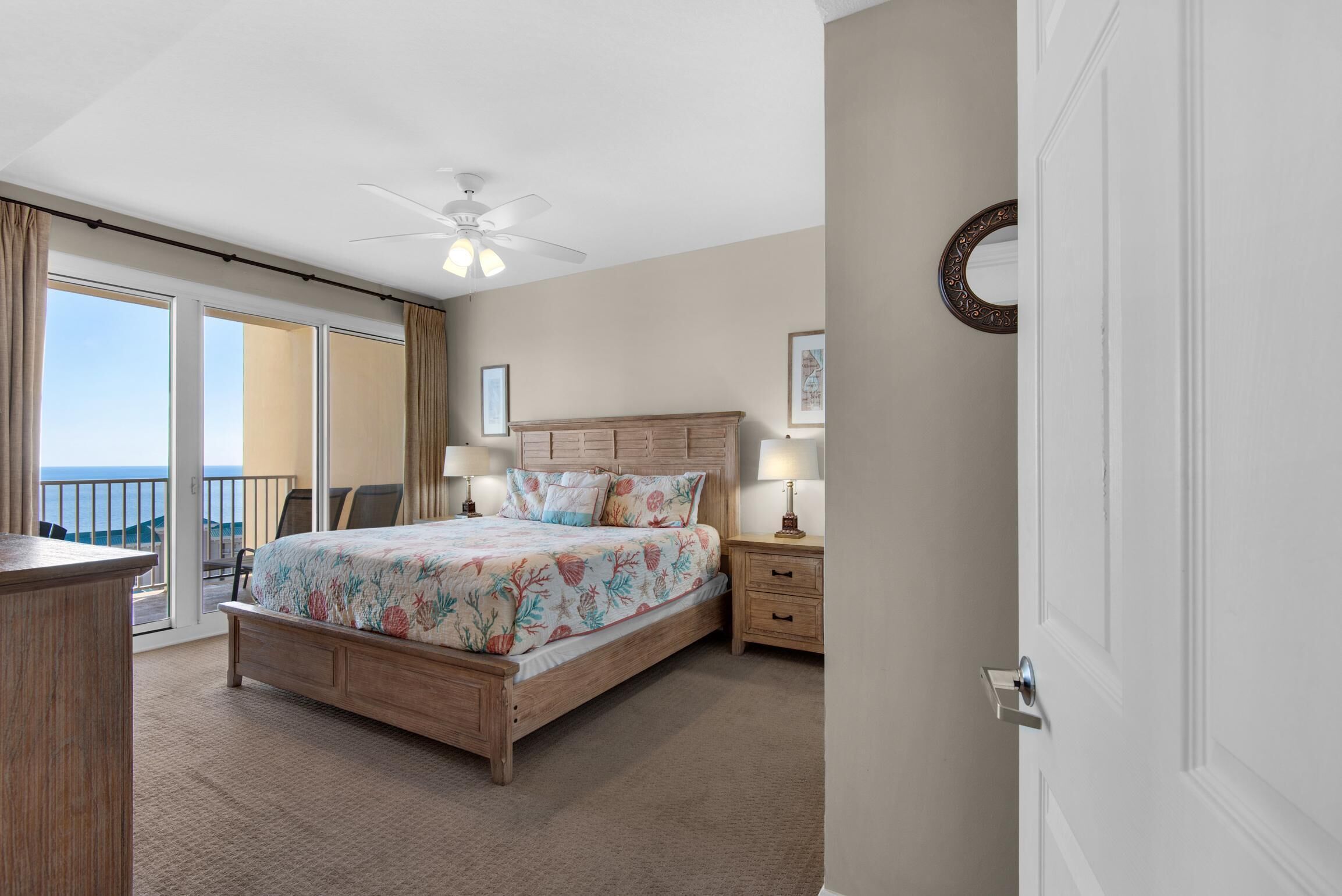 Une chambre à coucher avec un lit, des tables de chevet, un ventilateur de plafond et une vue sur l’extérieur.