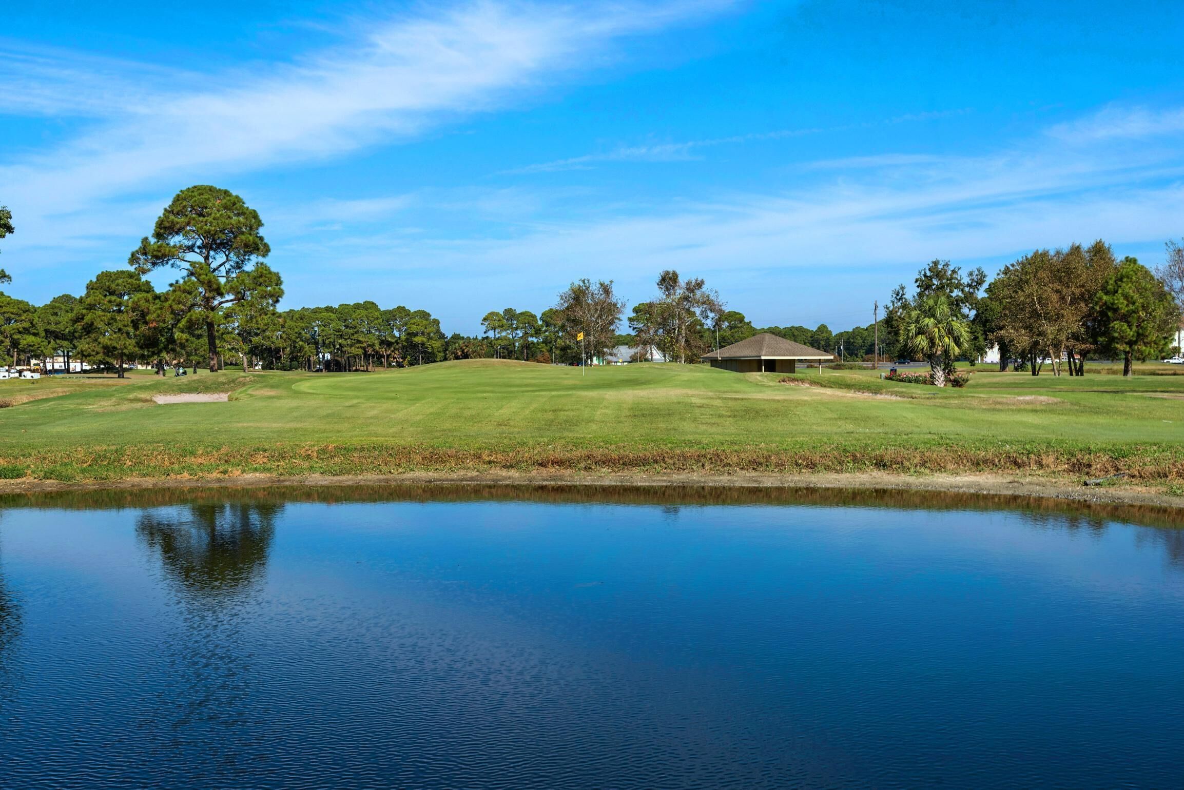 A golf course with a pond, trees, and a clubhouse.