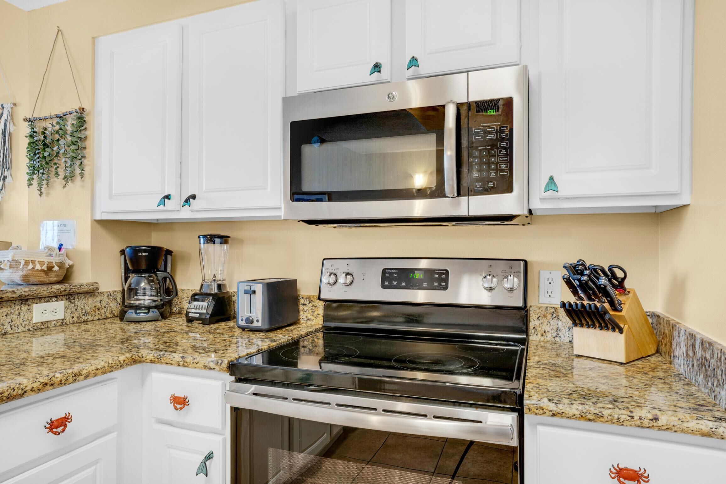 A kitchen with white cabinets, a stainless steel microwave, a stove, a coffee maker, and a knife block.