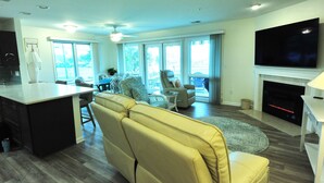 A spacious living area with a kitchen, a fireplace, a large TV, and a balcony with a view. - Waterfront in Historic Rock Hall, overlooking the main harbor and Chesapeake Bay (Rock Hall)