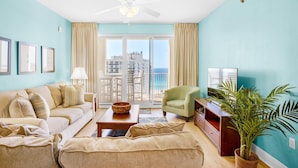 A living room with a sofa, armchair, and a plant. There is a balcony with a view of the ocean. - Ariel Dunes I 1502 (Miramar Beach)