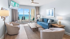 A modern living room with a sofa, armchairs, a coffee table, a TV, and a balcony with a view of the ocean. - Ariel Dunes I 1403 (Miramar Beach)