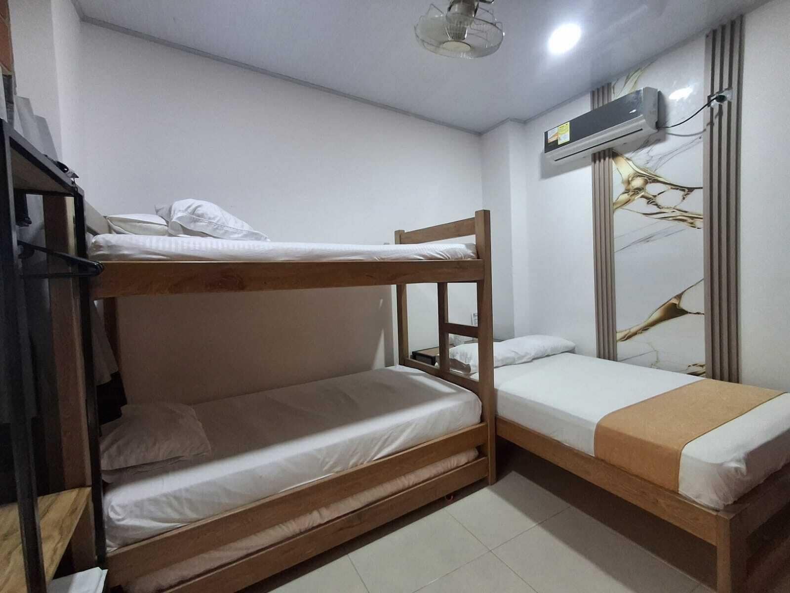 Una habitación pequeña con literas, ventilador de techo, aire acondicionado y una pared con diseño decorativo.