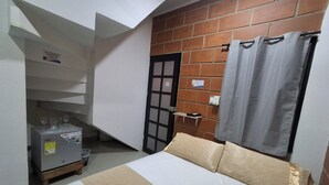 A small room with a bed, a brick wall, a door, and a small cabinet. - CABAÑAS MAR CARIBE (Necoclí)
