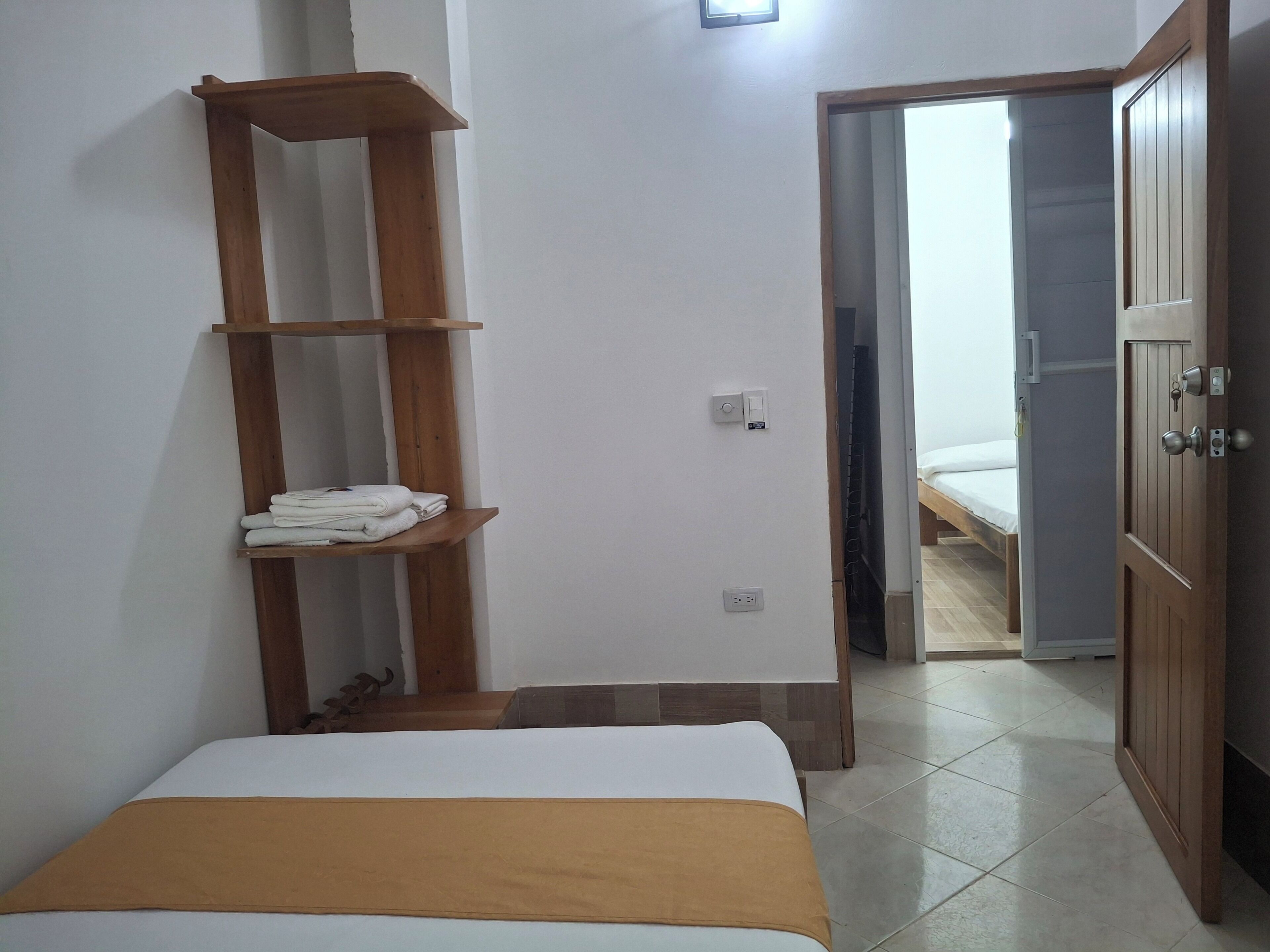 Une chambre à coucher avec un lit, une étagère en bois où sont rangées des serviettes, une armoire et une porte donnant sur une autre pièce.