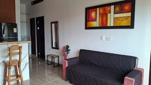 A modern living room with a black sofa, a wooden chair, a small table, and a decorative vase with flowers. - CABAÑAS MAR CARIBE (Necoclí)