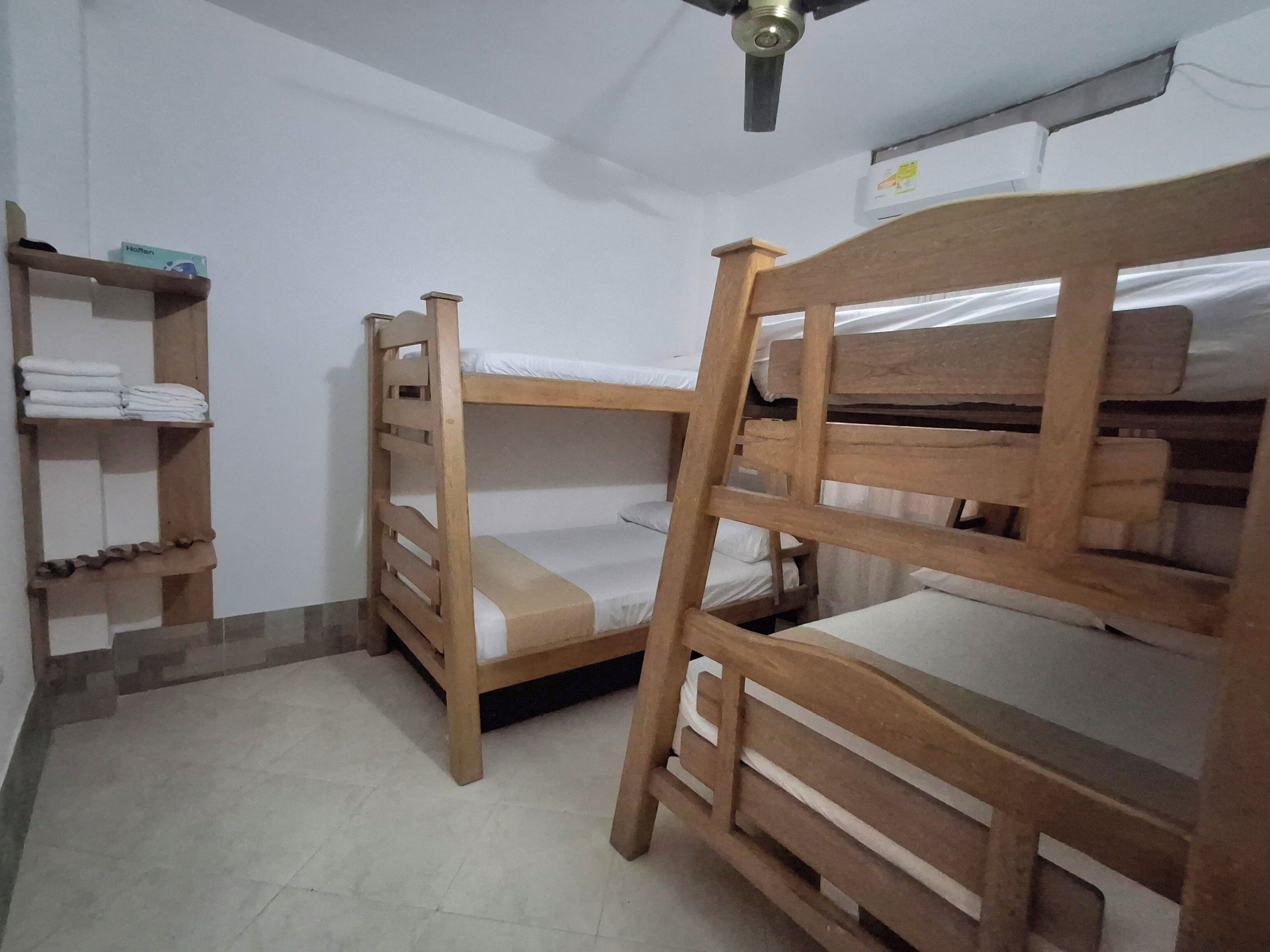 A room with two wooden bunk beds, a shelf with folded towels, and a ceiling fan.