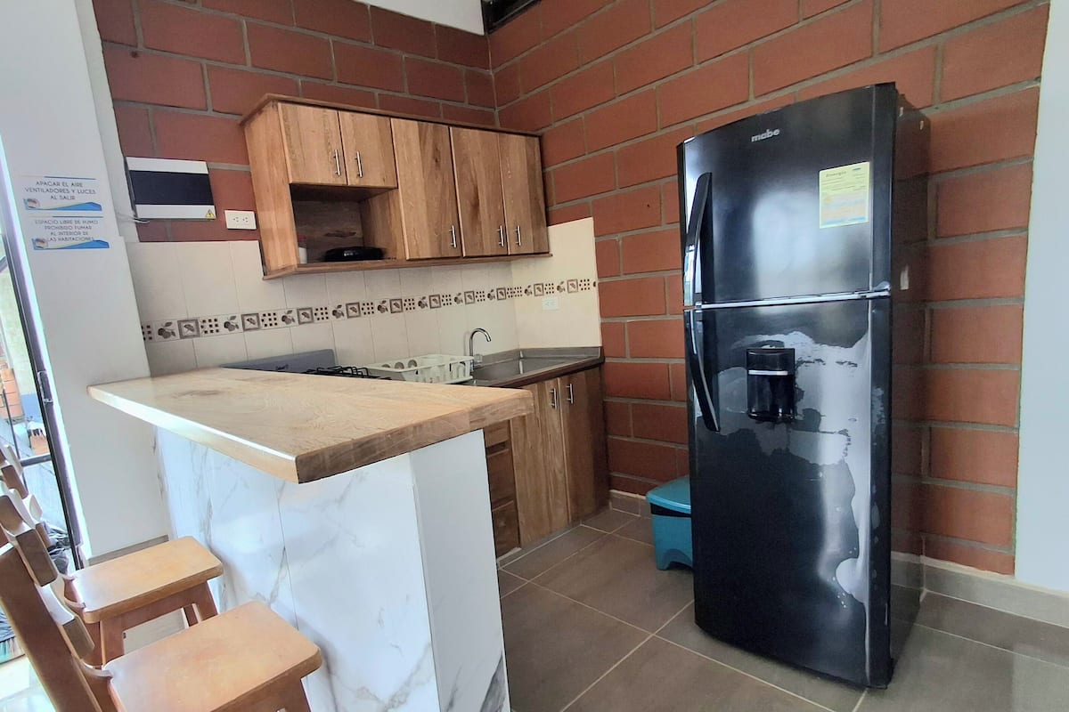 A kitchen with wooden cabinets, a marble countertop, a black refrigerator, and a sink.
