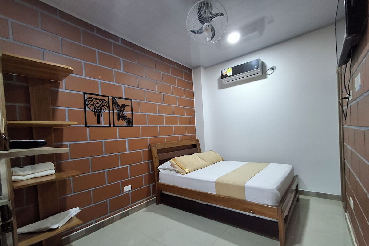 A room with a brick wall, a bed with a wooden frame, a ceiling fan, and an air conditioning unit.