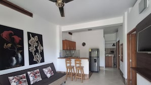 A modern living room with a sofa, chairs, a ceiling fan, and a kitchen area with cabinets and a refrigerator. - CABAÑAS MAR CARIBE (Necoclí)