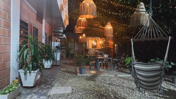 An outdoor seating area with tables and chairs, surrounded by potted plants and hanging lamps. - CABAÑAS MAR CARIBE (Necoclí)