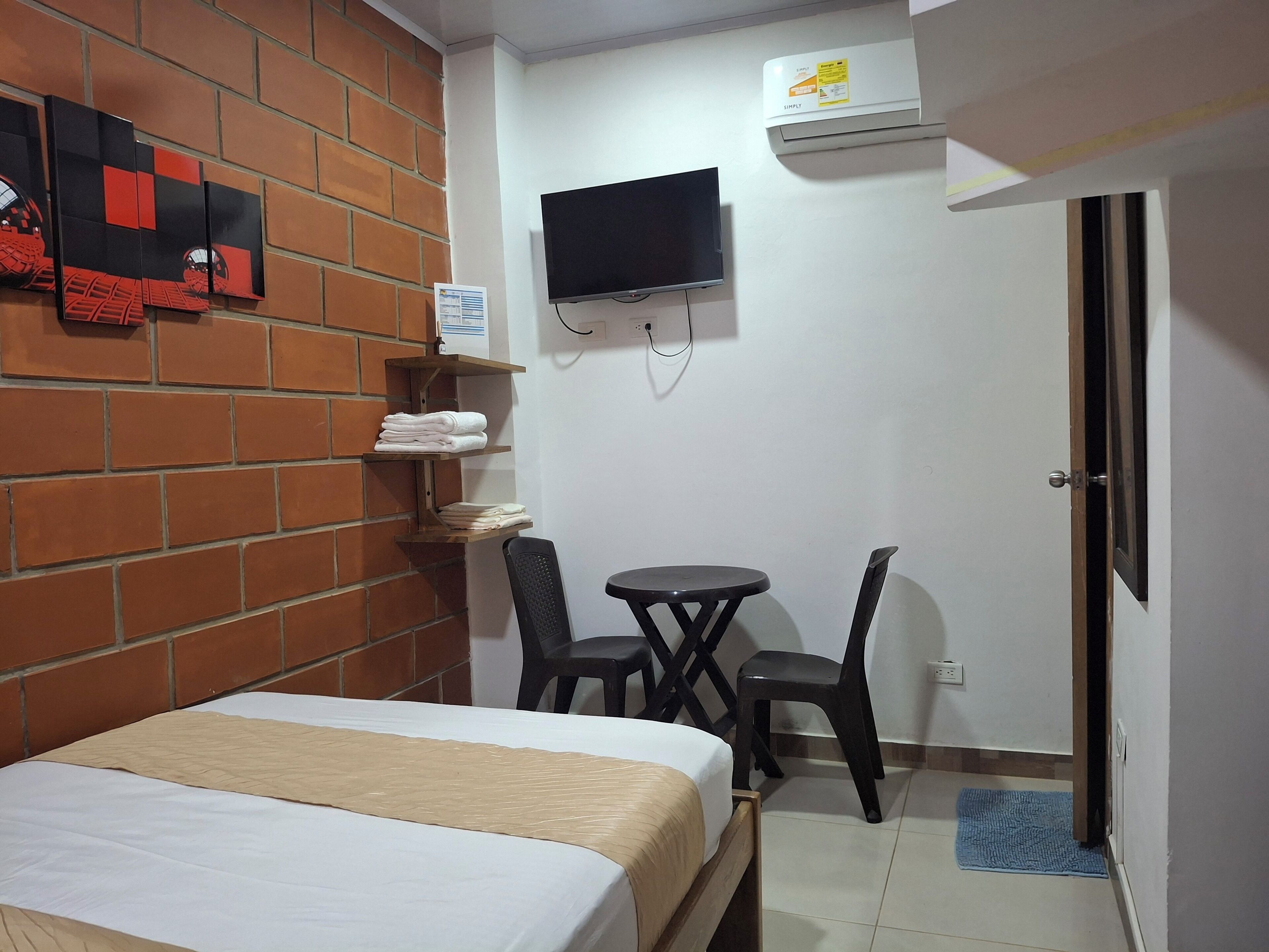 A room with a bed, a TV mounted on the wall, a small table with two chairs, and a door.