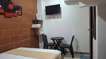A room with a bed, a TV mounted on the wall, a small table with two chairs, and a door.