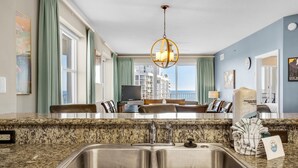 A modern kitchen with granite countertops, stainless steel sinks, and a dining area with a view of the city. - Ariel Dunes I 1401 (Miramar Beach)