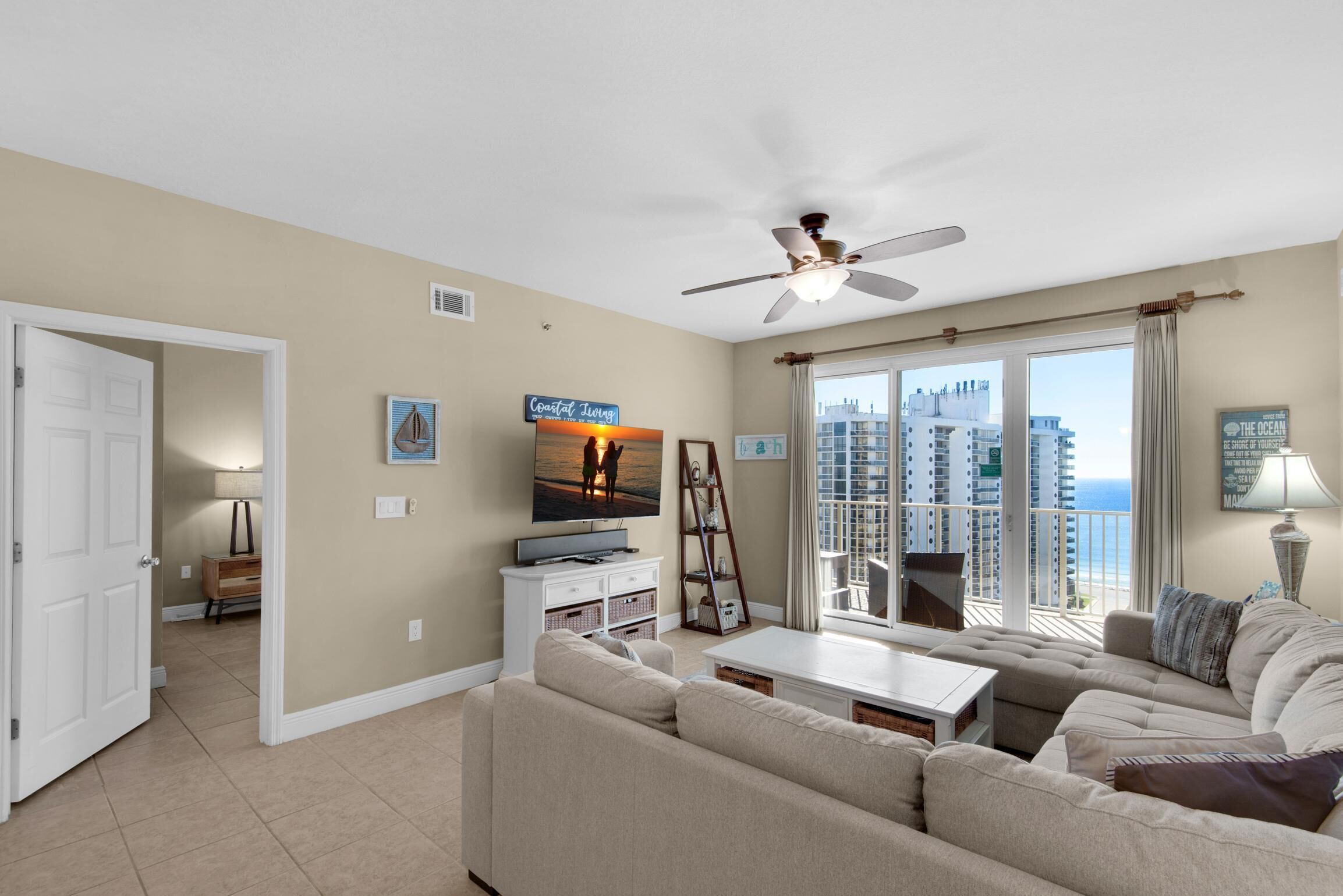 A living room with a sofa, a coffee table, a TV, and a balcony with a view of the city.