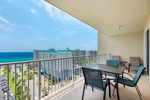 A balcony with a table and chairs, overlooking a beach and high-rise buildings. - Ariel Dunes I 1204 (Miramar Beach)