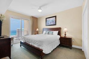 A bedroom with a large bed, a ceiling fan, a view of the ocean through a sliding door, and a wooden dresser. - Ariel Dunes I 1204 (Miramar Beach)