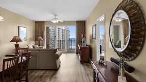 A spacious living room with a balcony, a dining area, and a large mirror. - Ariel Dunes I 1204 (Miramar Beach)
