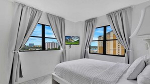 A modern hotel room with a large bed, two windows with curtains, a flat-screen TV, and a city view. - INTERNATIONAL dr/UNIVERSAL 2 Bedroom CONDO-HOTEL (Orlando)