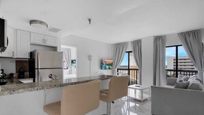 A modern apartment with a kitchen, dining area, and living room. It features a large window with curtains, a flat-screen TV, and a balcony with a view. - INTERNATIONAL dr/UNIVERSAL 2 Bedroom CONDO-HOTEL (Orlando)