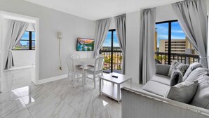 A modern living room with a balcony, a dining area, and a TV mounted on the wall. - INTERNATIONAL dr/UNIVERSAL 2 Bedroom CONDO-HOTEL (Orlando)