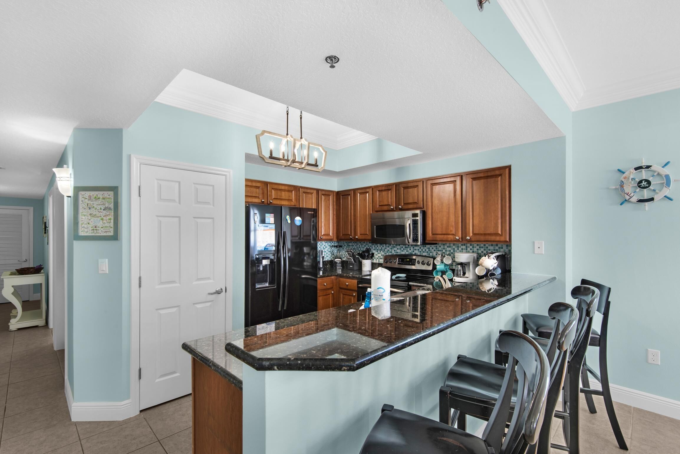 A kitchen with wooden cabinets, a black refrigerator, a microwave, and a stainless steel oven. There is a large island with a sink and bar stools.