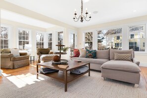 A spacious living room with large windows, a chandelier, and a cozy seating area.