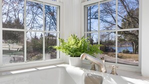 A bathroom with a white sink, two faucets, and a window with a view of trees and a body of water. - Picturesque Home with Harbor Views! (Kennebunkport)