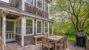A wooden deck with a table and chairs, a barbecue grill, and a covered bench area. - Picturesque Home with Harbor Views! (Kennebunkport)