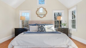 A bedroom with a large bed, two nightstands, a mirror, and windows. - Picturesque Home with Harbor Views! (Kennebunkport)