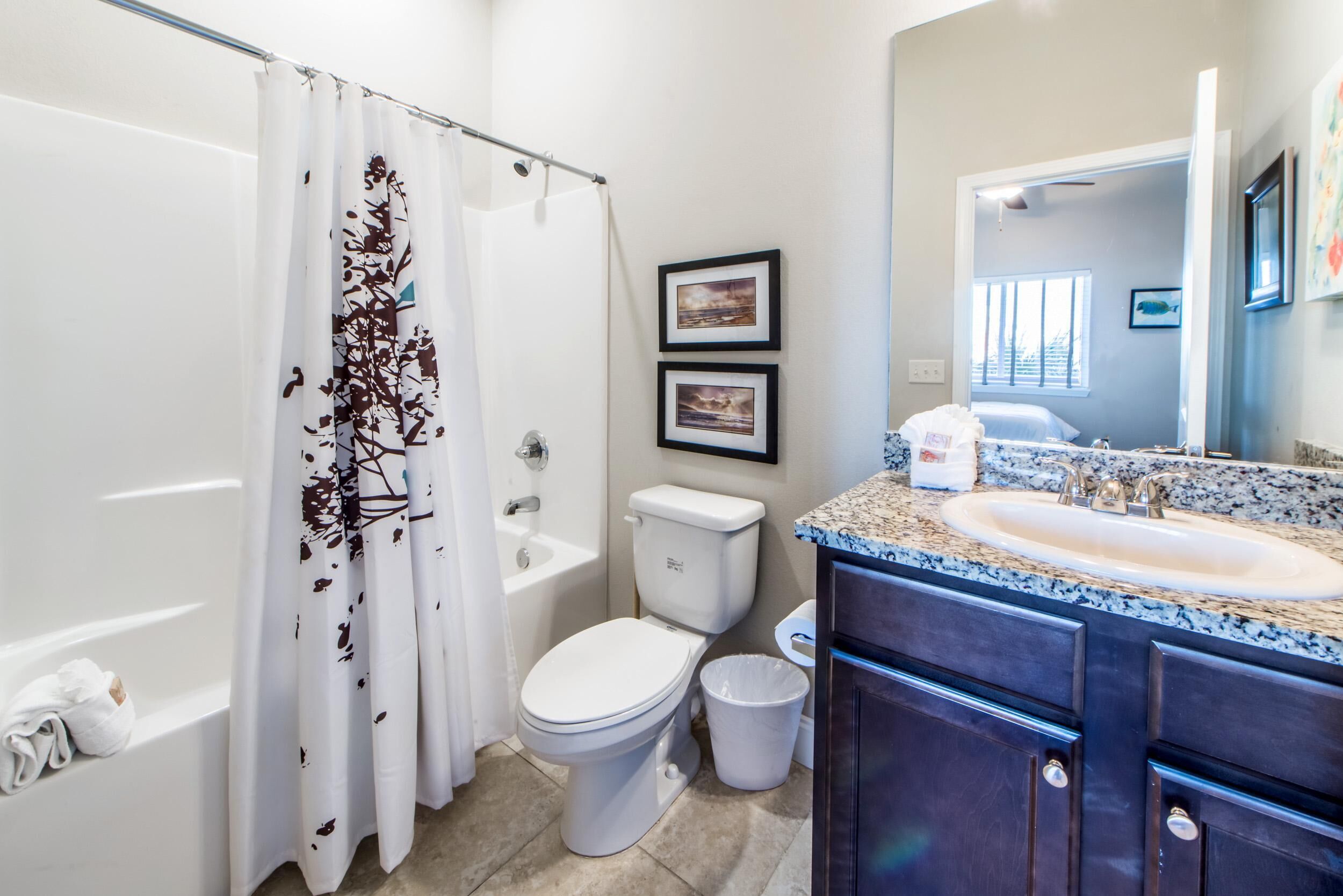 A bathroom with a shower curtain, toilet, sink, and vanity.