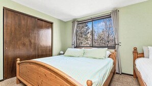 Quarto com cama de madeira, janela com cortinas e guarda-roupa.