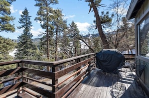 A wooden deck with a barbecue grill and outdoor furniture, overlooking a forested area.