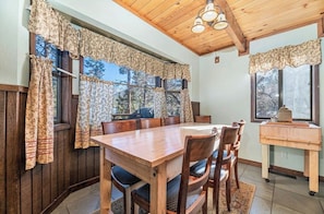 A dining area with a wooden table and chairs, large windows with floral curtains, and a ceiling with wooden beams and lights. - Ski slope views, Short walk to Bear Mtn and hiking trails. Great for all seasons (Big Bear Lake)