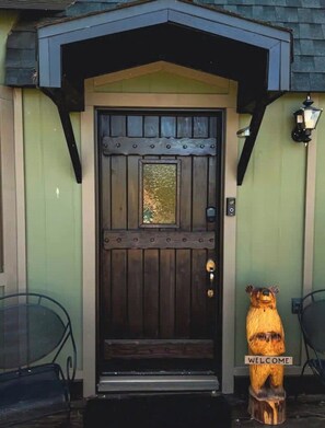 A wooden door with a 'WELCOME' sign, a metal bench, and a lamp post.
