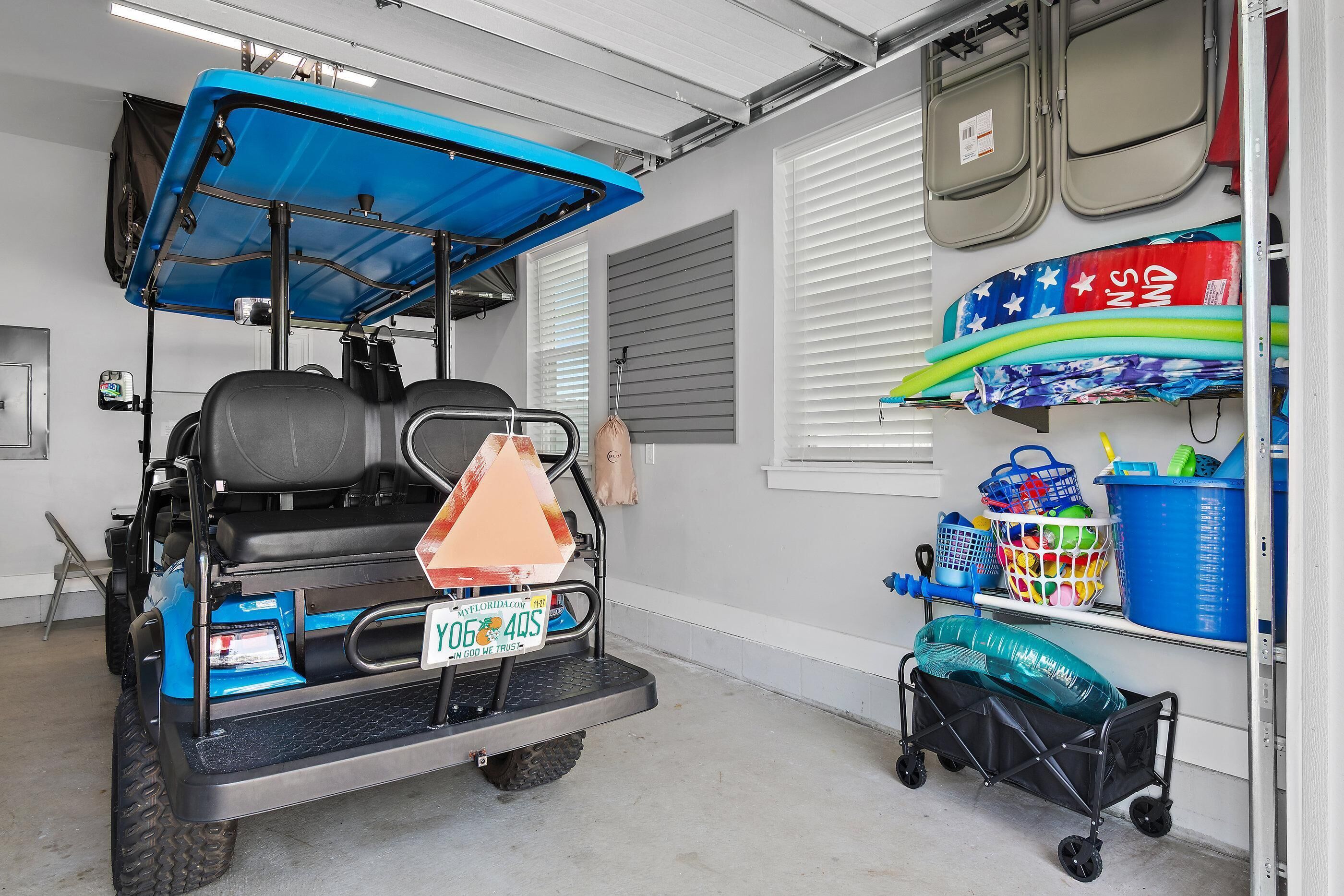 Un garage contenant une voiturette de golf bleue, une poussette et des étagères de rangement remplies de divers objets.