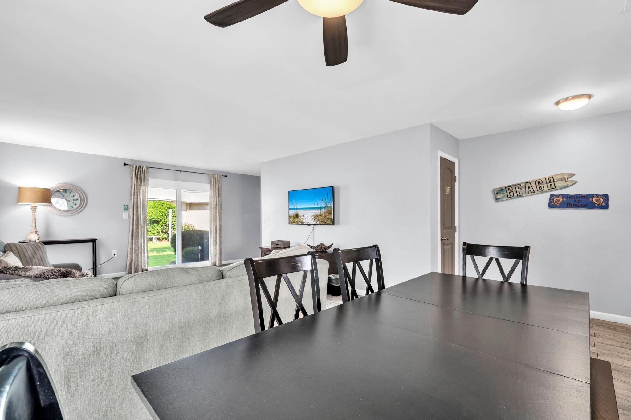 A modern living room with a dining area, a ceiling fan, a TV, and a view of the outdoors.