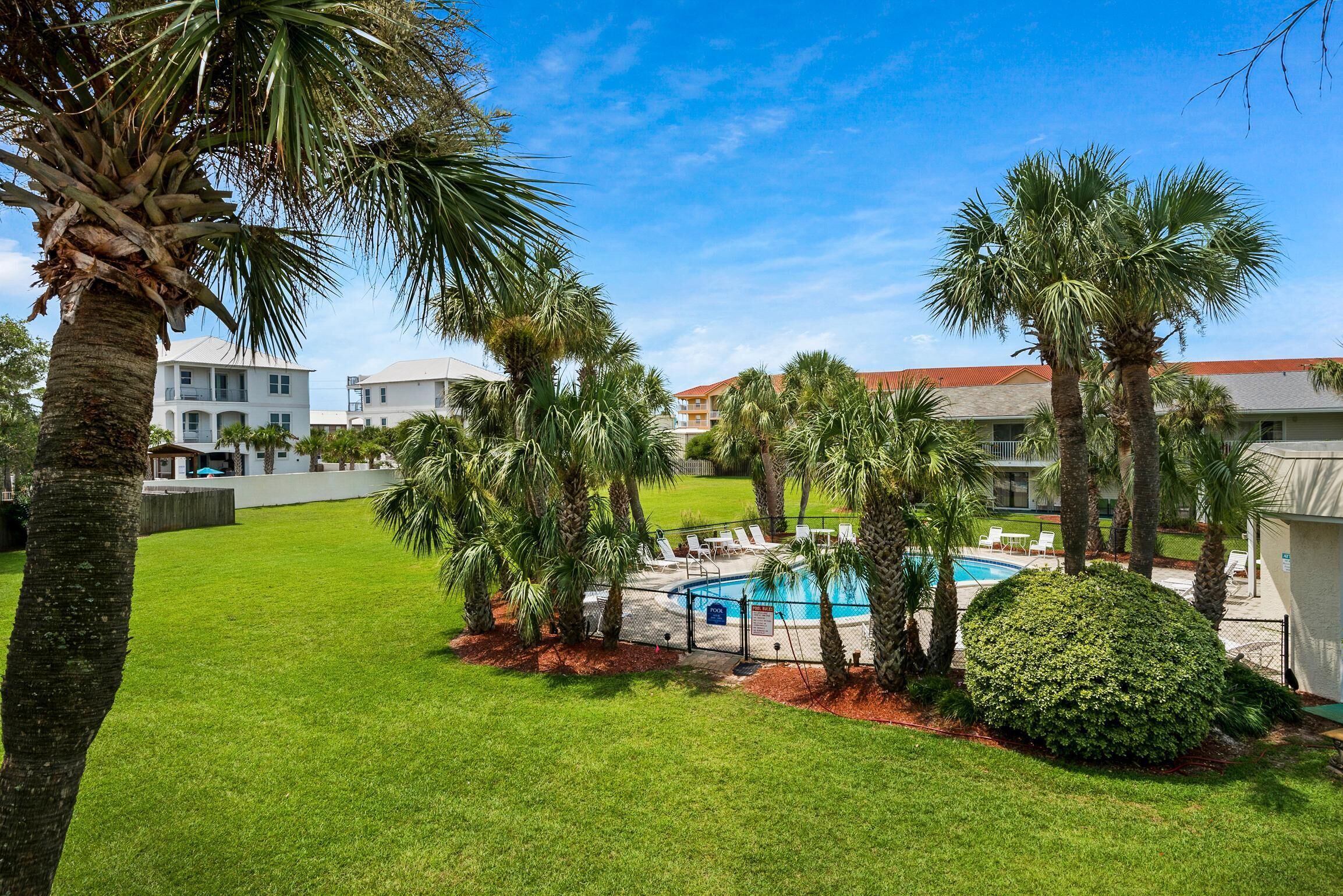 A pool area with palm trees, a well-maintained lawn, and a clear blue sky.