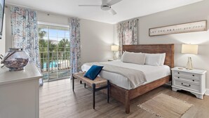 A bedroom with a large bed, a nightstand, a bench, a ceiling fan, and a view of a pool through a glass door. - Summerhouse Townhomes #5 (Miramar Beach)